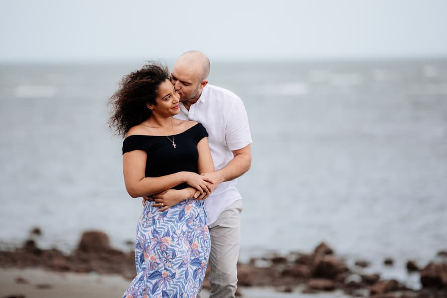 Couple embracing on the beach with the sea in the background.