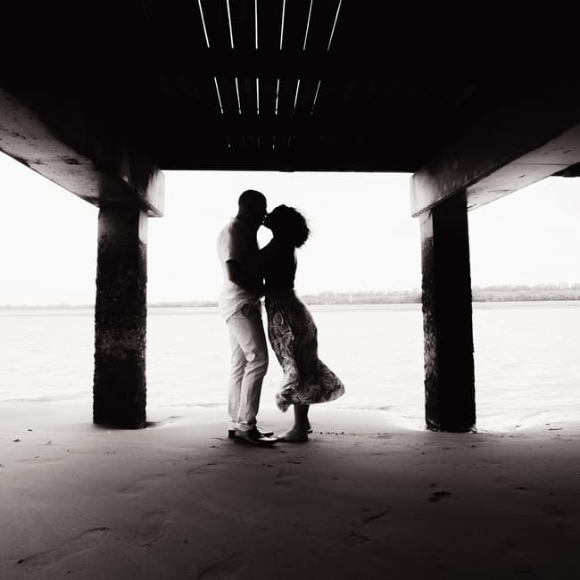 Silhouette of the couple under a pier at Shorncliffe beachfront, with the ocean in the background.