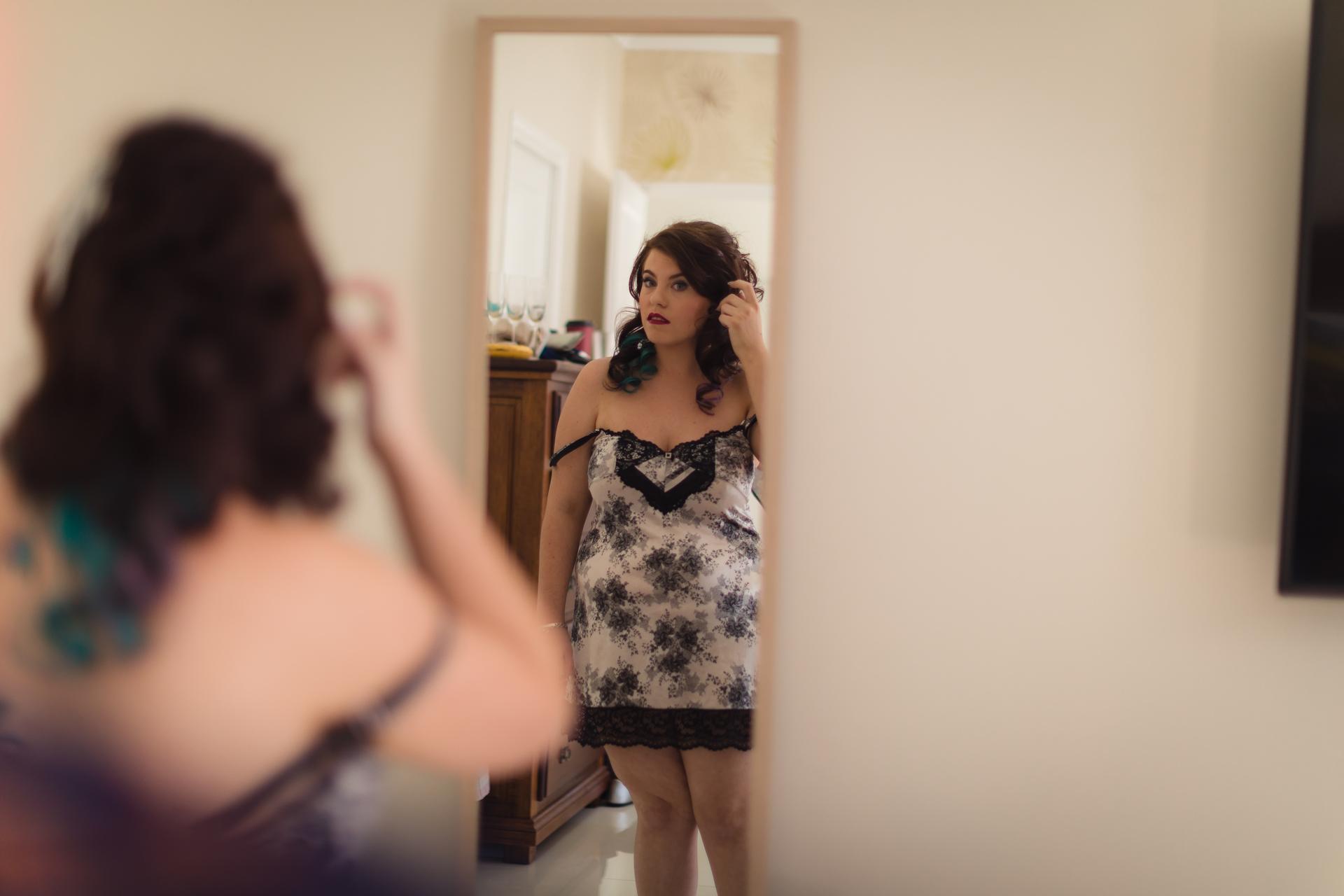 The bride Holly is seen adjusting her hair while looking at herself in a mirror during bridal preparation.