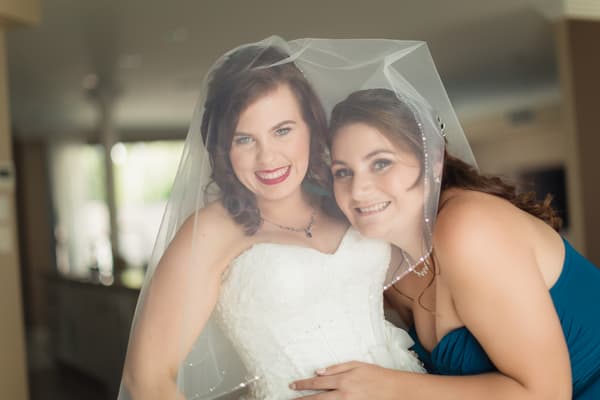 The bride Holly in her wedding dress and veil poses closely with a bridesmaid in a blue dress. Wedding photographers Brisbane by She Said Yes.