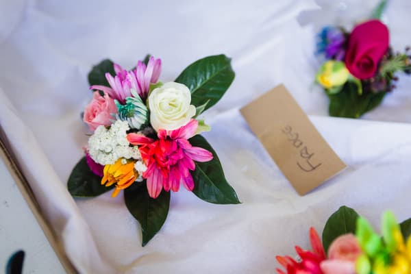 Close-up of colorful floral boutonnieres arranged on white fabric at Kwila Lodge, one labeled 'Fraser'.