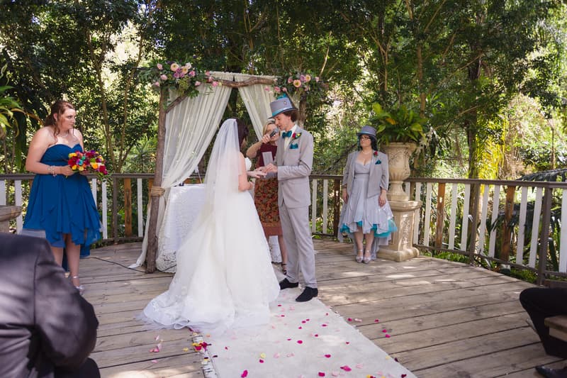 Bride Holly and groom Paul exchange rings during their wedding ceremony at Kwila Lodge, with the officiant standing behind them and two attendants nearby.