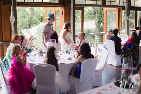 The bride Holly and the groom Paul enter the reception area at Kwila Lodge, greeted by seated guests applauding around decorated tables.