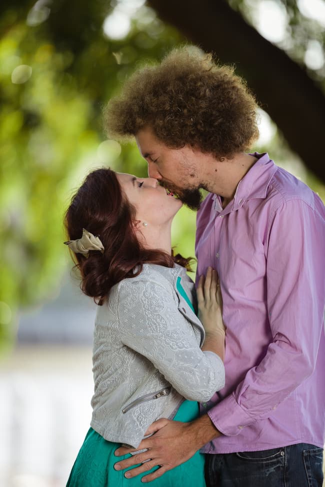 Couple standing close, looking into each other's eyes, surrounded by greenery.