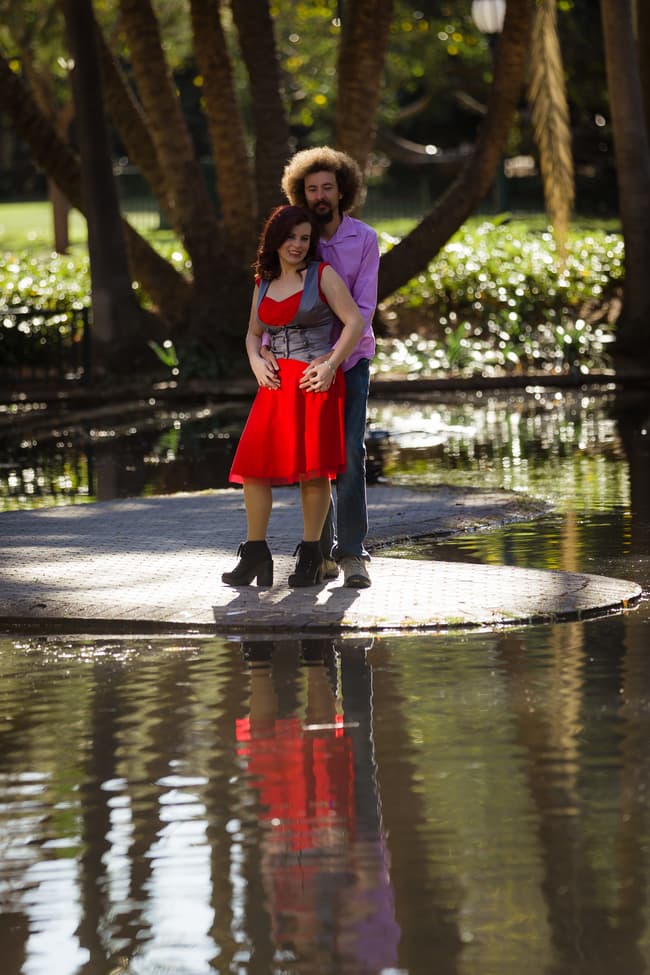 Couple standing by a pond, one looking up at the other, both smiling warmly.
