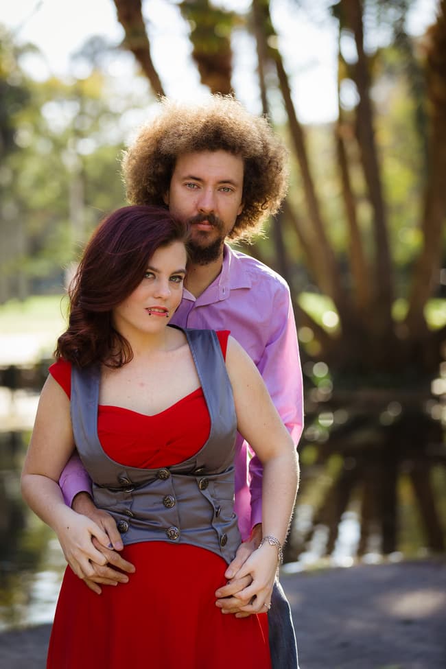 Couple standing on a platform over water, embracing with trees in the background.