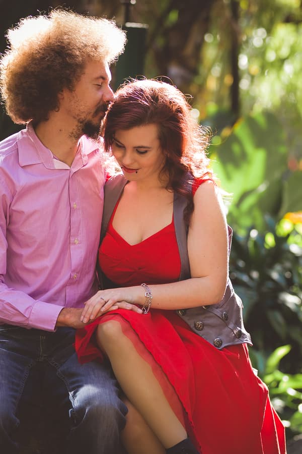 The couple sits on a stone ledge surrounded by lush greenery in City Botanic Gardens, Brisbane, sharing an intimate moment.