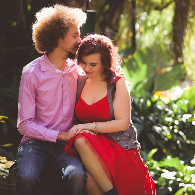 The couple sits on a stone ledge surrounded by lush greenery in City Botanic Gardens, Brisbane, sharing an intimate moment.