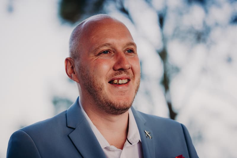 The groom Arran is shown smiling in a close-up portrait at Sandstone Point Hotel — Pavilion during the ceremony stage.