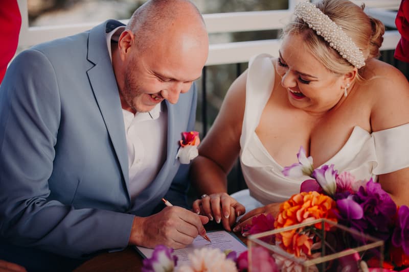 Jacquelyne and Arran sign the wedding register at Sandstone Point Hotel — Pavilion during the ceremony stage.