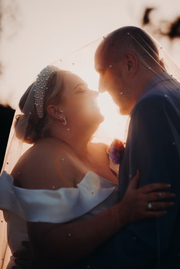 Bride Jacquelyne and groom Arran embrace closely under the bride's veil at Sandstone Point Hotel during their couple portraits session.