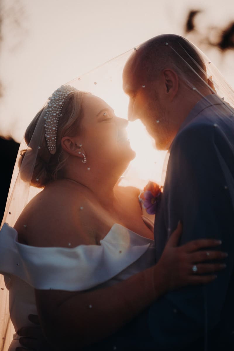 Bride Jacquelyne and groom Arran embrace closely under the bride's veil at Sandstone Point Hotel during their couple portraits session.