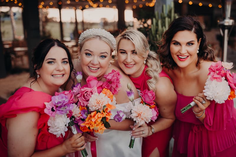 The bride Jacquelyne poses with three bridesmaids at Sandstone Point Hotel, all holding colorful bouquets and smiling at the camera.