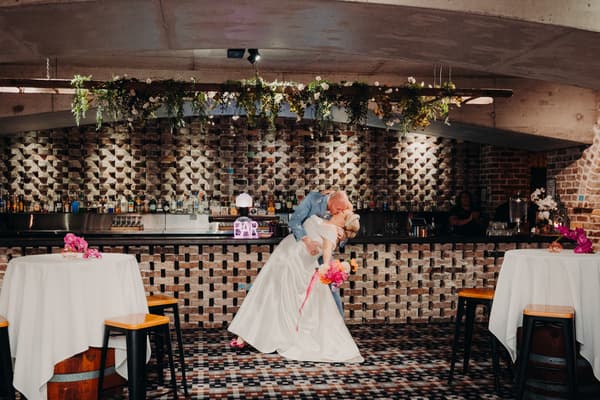 Bride Jacquelyne and groom Arran share a kiss in a dip pose in front of the bar at Sandstone Point Hotel — Cellar during the reception stage.