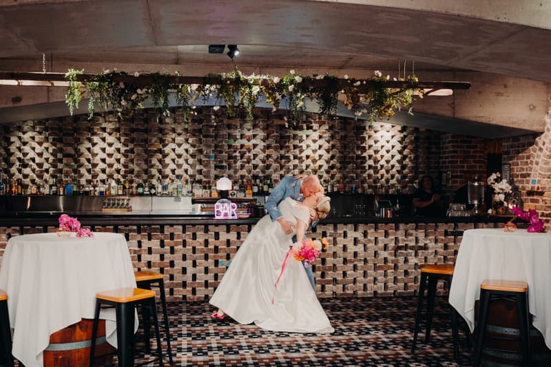Bride Jacquelyne and groom Arran share a kiss in a dip pose in front of the bar at Sandstone Point Hotel — Cellar during the reception stage.