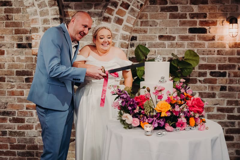 Jacquelyne and Arran cut their wedding cake decorated with colorful flowers at Sandstone Point Hotel — Cellar.