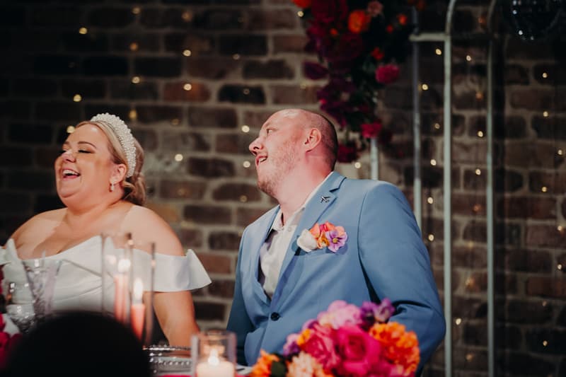Bride Jacquelyne and groom Arran sit at a decorated table with candles and floral arrangements at the Sandstone Point Hotel — Cellar during the reception stage.