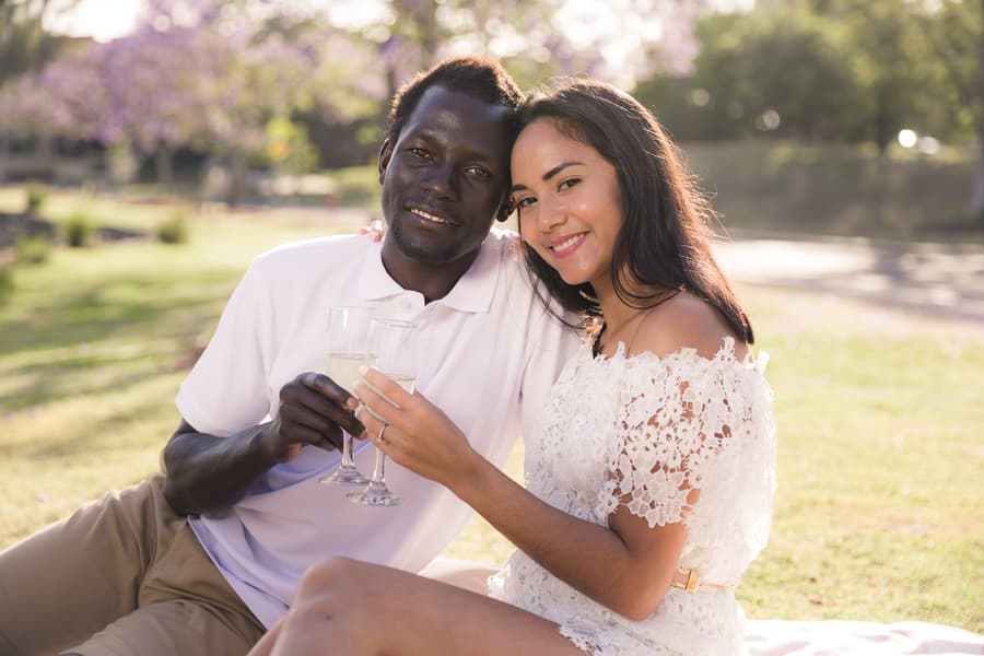 The couple sitting on a blanket, surrounded by jacaranda trees, with one gently touching the other's face.