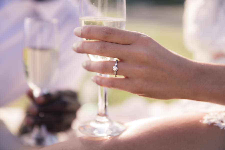 The couple on a picnic blanket, pouring champagne, with sunlight filtering through the trees.