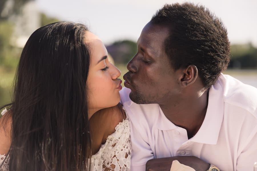The couple leaning in for a kiss on a sunny day at UQ Lakes, with a playful expression.
