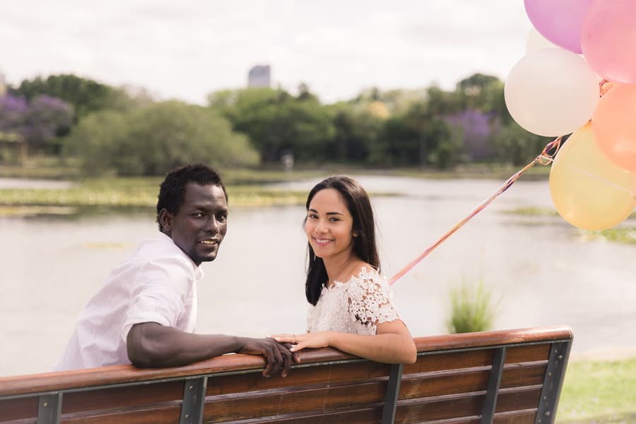 The couple sitting on a bench, turning to smile at the camera with balloons in hand.