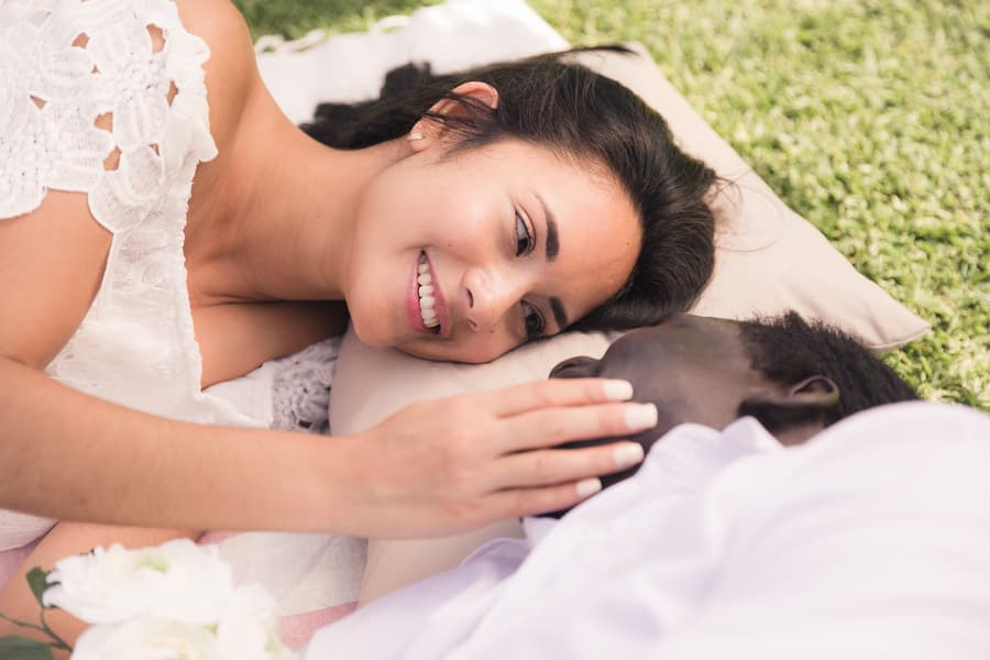 A woman lying on a blanket, smiling and touching a man's face gently, with a bouquet of white flowers beside her.