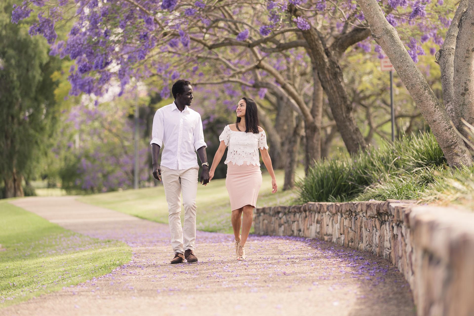 A couple walking hand in hand along a path lined with jacaranda trees in bloom, creating a romantic atmosphere.