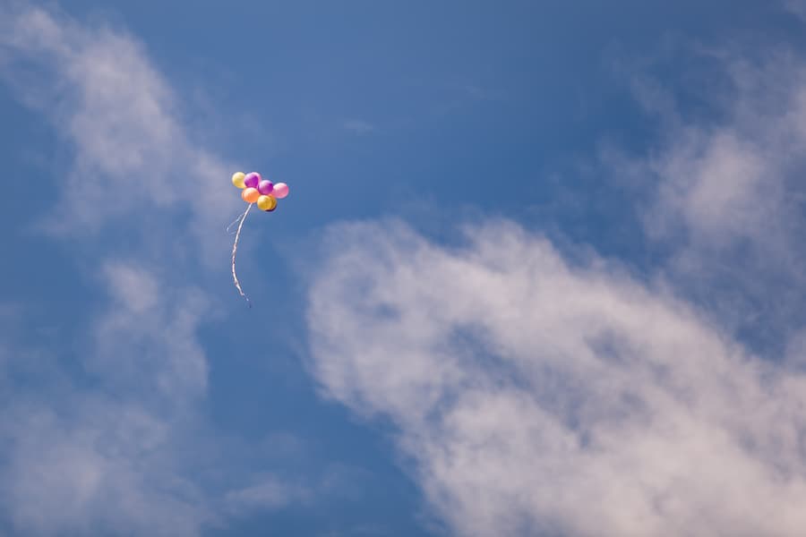 Colorful balloons floating high in a blue sky with scattered clouds, creating a whimsical scene.