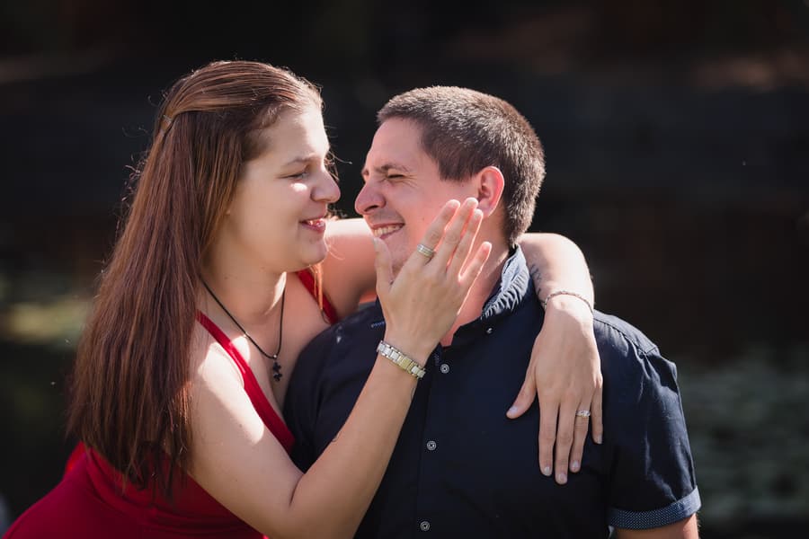 The woman gently touches the man's face as they both smile, enjoying a tender moment in the garden.