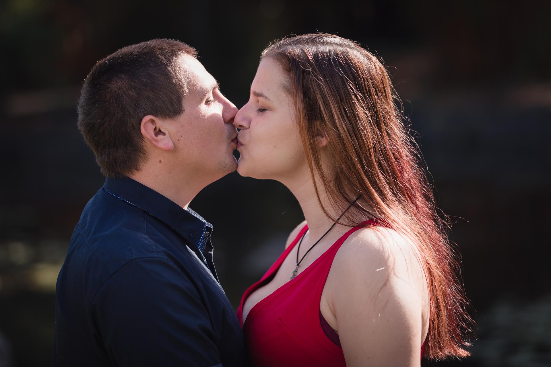 The couple shares a kiss, standing closely together with soft sunlight illuminating them.