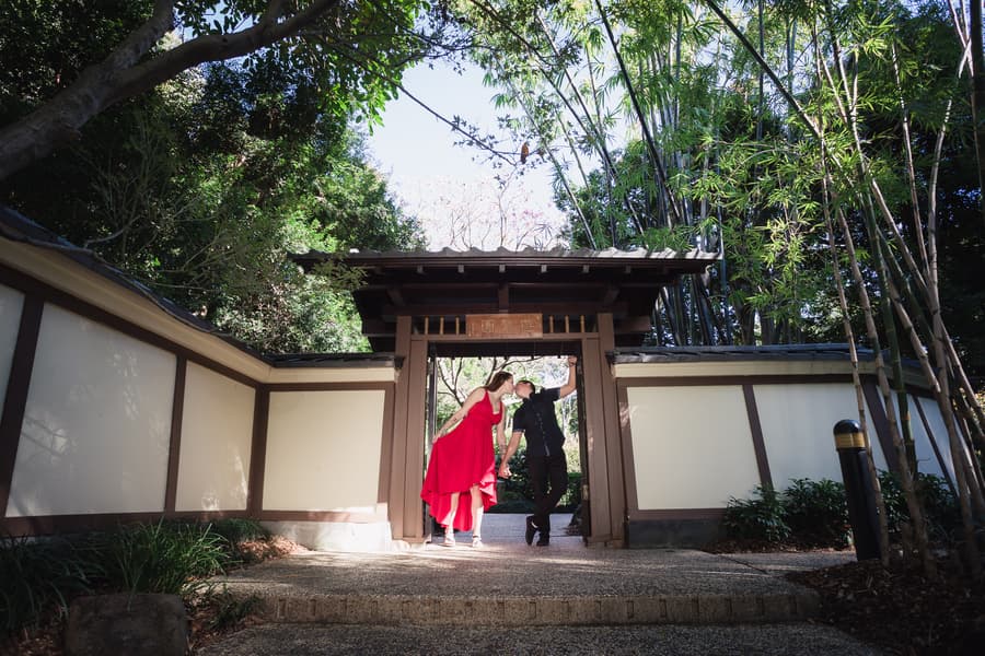 The couple shares a playful moment, holding hands and smiling, under a traditional Japanese gate.