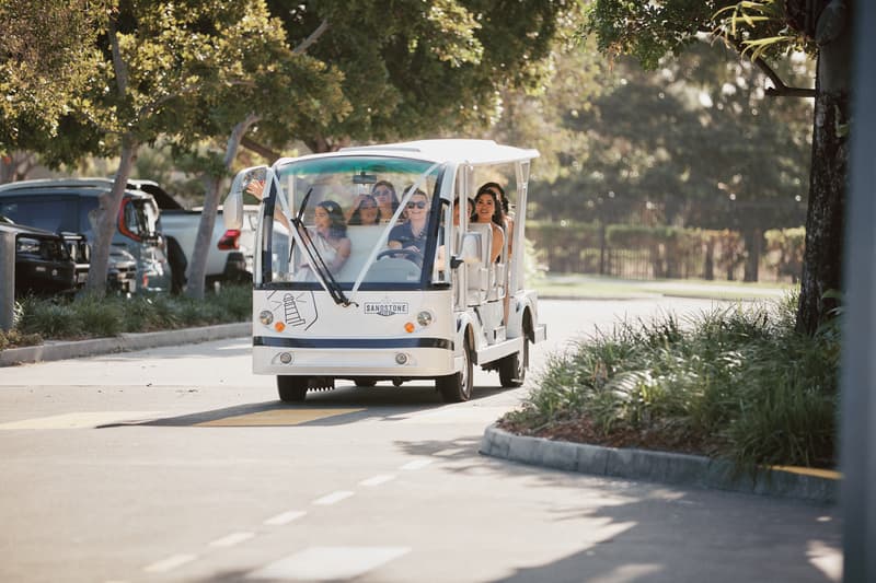 The bride Jheng and bridesmaids ride in a white electric shuttle cart at Sandstone Point Hotel — The Pavilion, surrounded by trees and parked cars.
