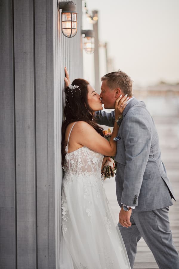 The bride Jheng and groom Dane share a kiss while standing close to a wooden wall with outdoor lights at Sandstone Point Hotel during their couple portraits session.