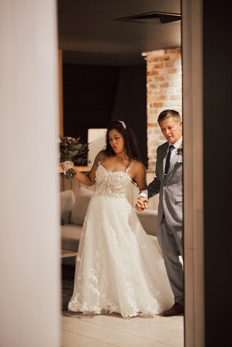 The bride Jheng in a white lace wedding gown holding a bouquet and the groom Dane in a gray suit holding hands inside the Pumicestone Room. Good wedding vows by She Said Yes.