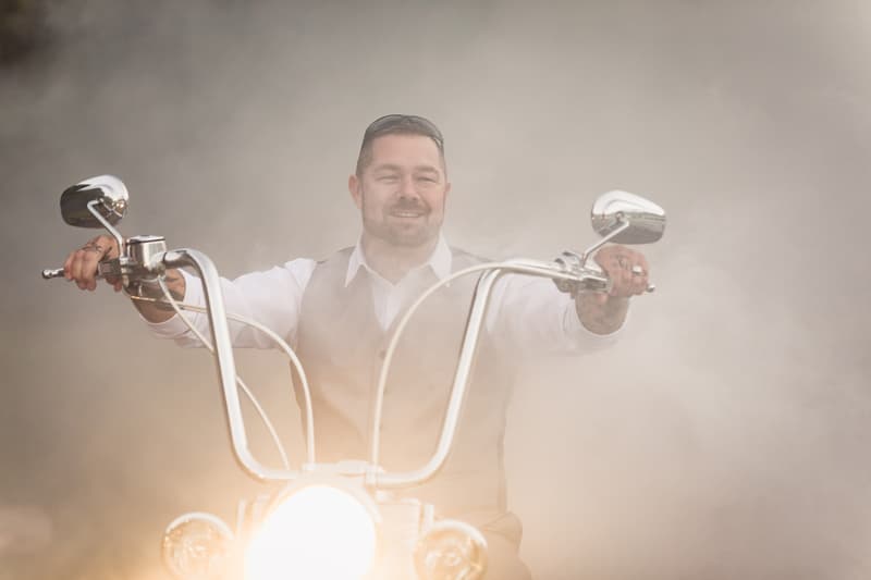 The groom Shane rides a motorcycle with the headlight on, surrounded by smoke at Novotel Sunshine Coast Resort.