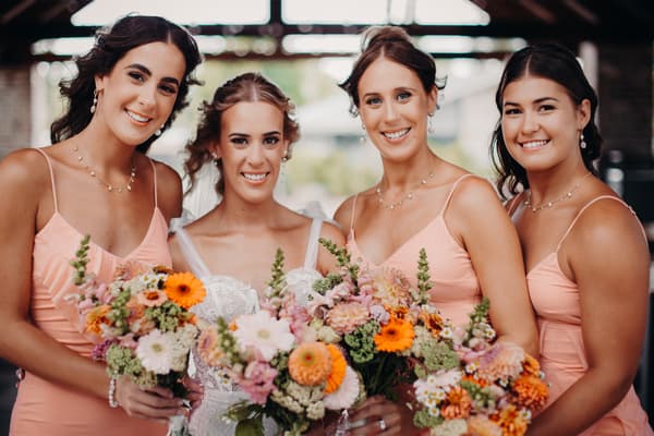 The bride Krystal poses with three bridesmaids holding bouquets of flowers. Spring wedding Queensland venues by She Said Yes.
