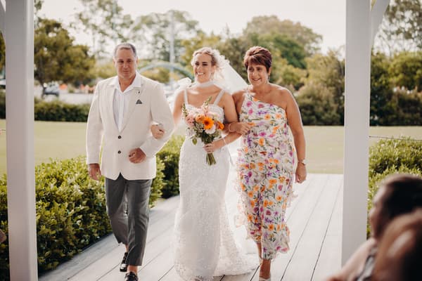 The bride Krystal walks arm-in-arm with the father and mother of the bride at Sandstone Point Hotel — Pavilion.