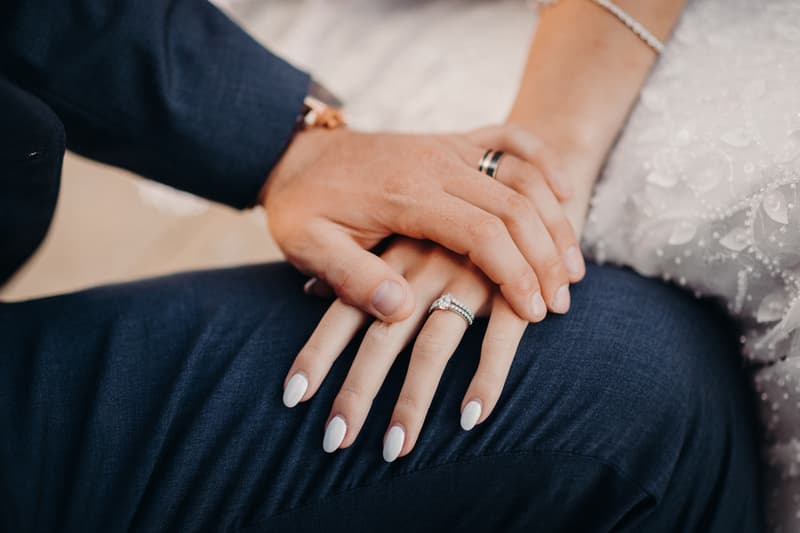 The bride and groom at Sandstone Point Hotel with their hands gently placed together, showing the bride's engagement and wedding rings and the groom's wedding band.