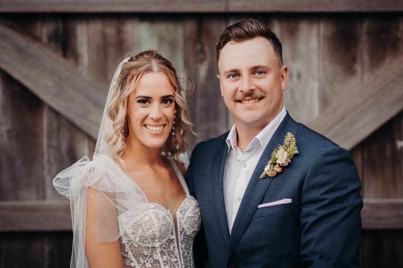 Bride Krystal and groom Brandon pose together in front of a wooden backdrop at Sandstone Point Hotel during their couple portraits session.