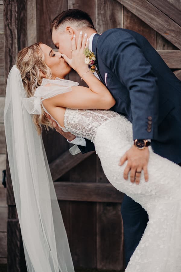 Bride Krystal and groom Brandon share a kiss as Brandon dips Krystal in front of a wooden door at Sandstone Point Hotel.