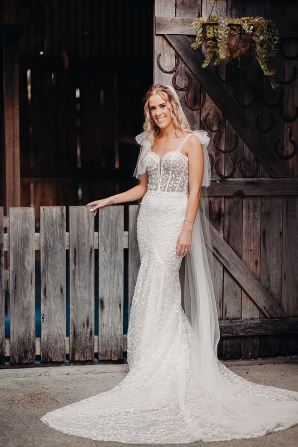The bride Krystal poses alone in her wedding gown in front of a rustic wooden fence and gate at Sandstone Point Hotel.