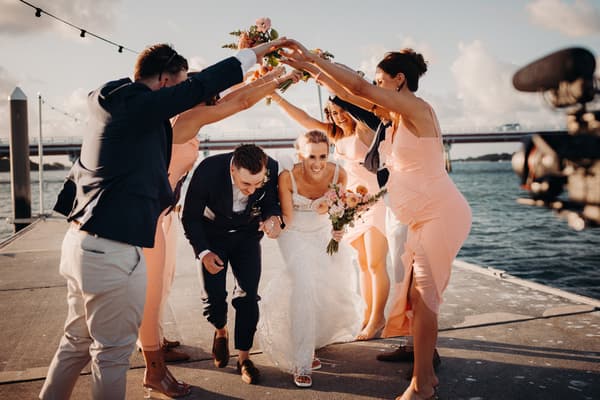 Krystal the bride and Brandon the groom crouch and smile as they pass under an arch formed by bridesmaids and groomsmen holding their arms up. Engagement reception by She Said Yes.