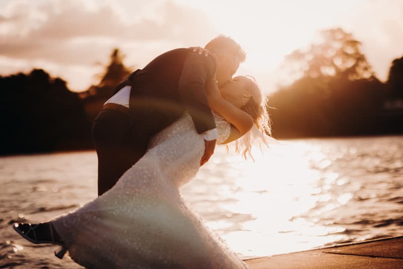 Bride Krystal and groom Brandon share a kiss in a dip pose by the water at Sandstone Point Hotel during their couple portraits session at sunset.