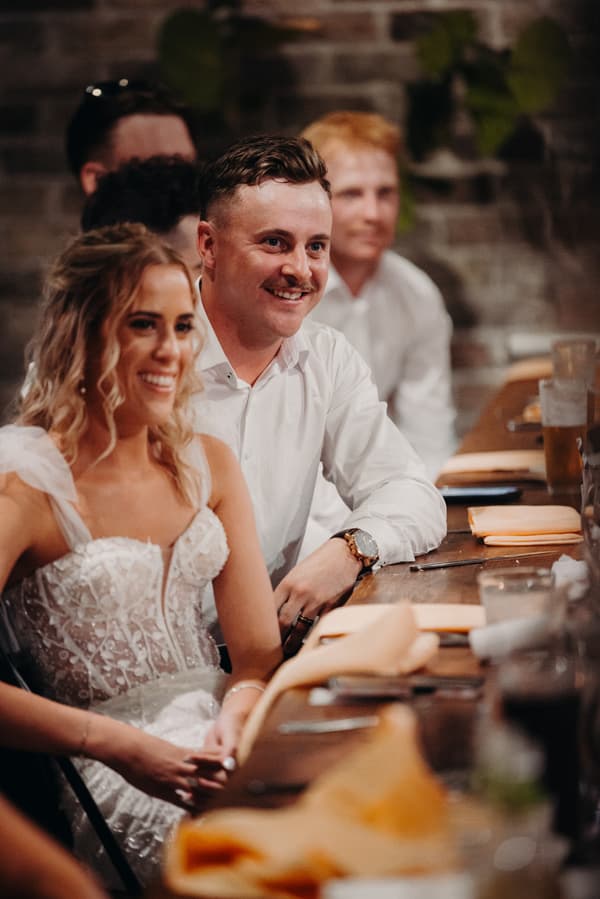 Bride Krystal and groom Brandon sit at a table with guests during the reception at Sandstone Point Hotel — Cellar.