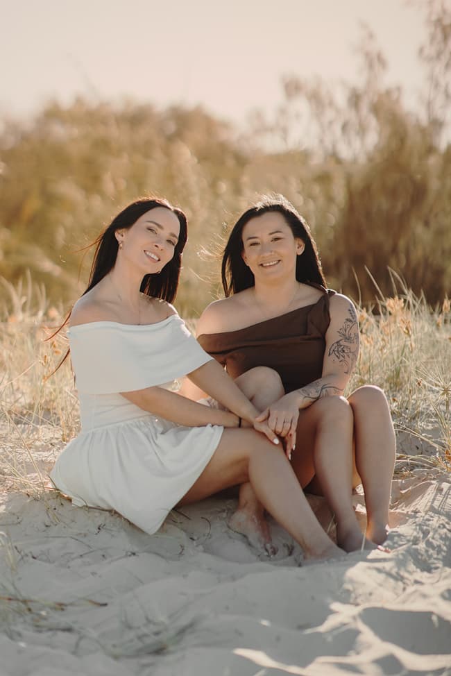 The couple sitting on the sand at Woorim Beach, smiling at the camera with relaxed and happy expressions.