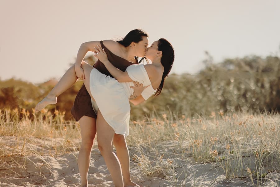 One person carrying the other in their arms, both sharing a kiss on the sandy dunes at Woorim Beach.