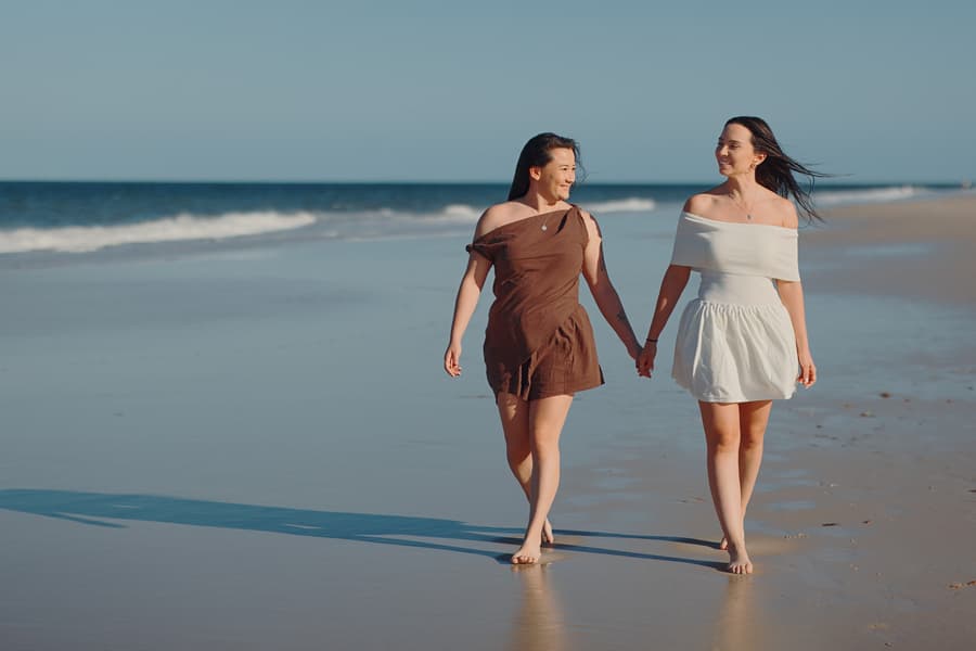 The couple walking hand in hand along the shoreline at Woorim Beach, with waves gently lapping at their feet.