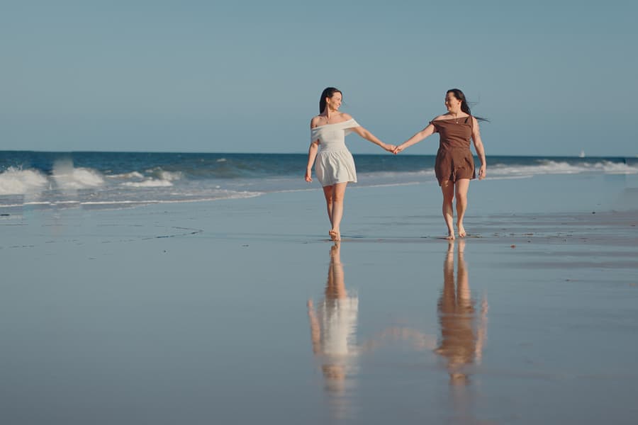 The couple walking towards each other on the wet sand at Woorim Beach, holding hands and smiling.