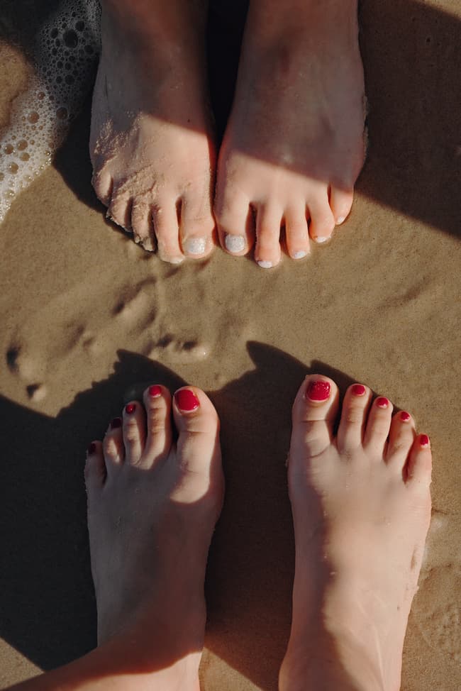 Close-up of the couple's feet in the wet sand at Woorim Beach, showing painted toenails and gentle waves.