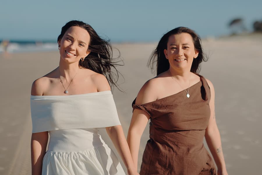 The couple walking closely together, smiling warmly at the camera, with the ocean in the background at Woorim Beach.